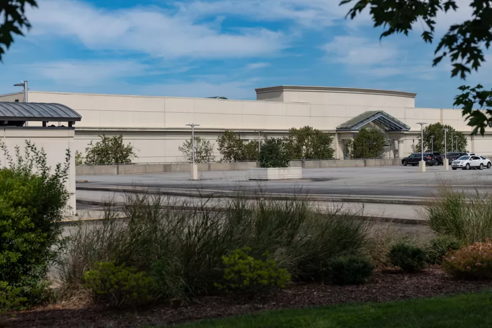 Large blank mall building with only two cars in large parking lot.